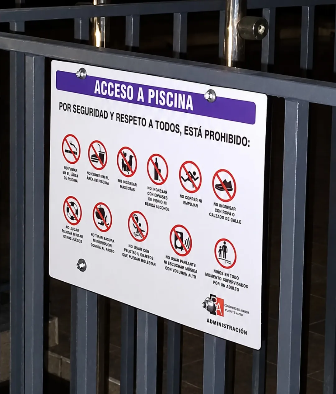 Letrero «Acceso a piscina» con normas de seguridad, instalado en una reja